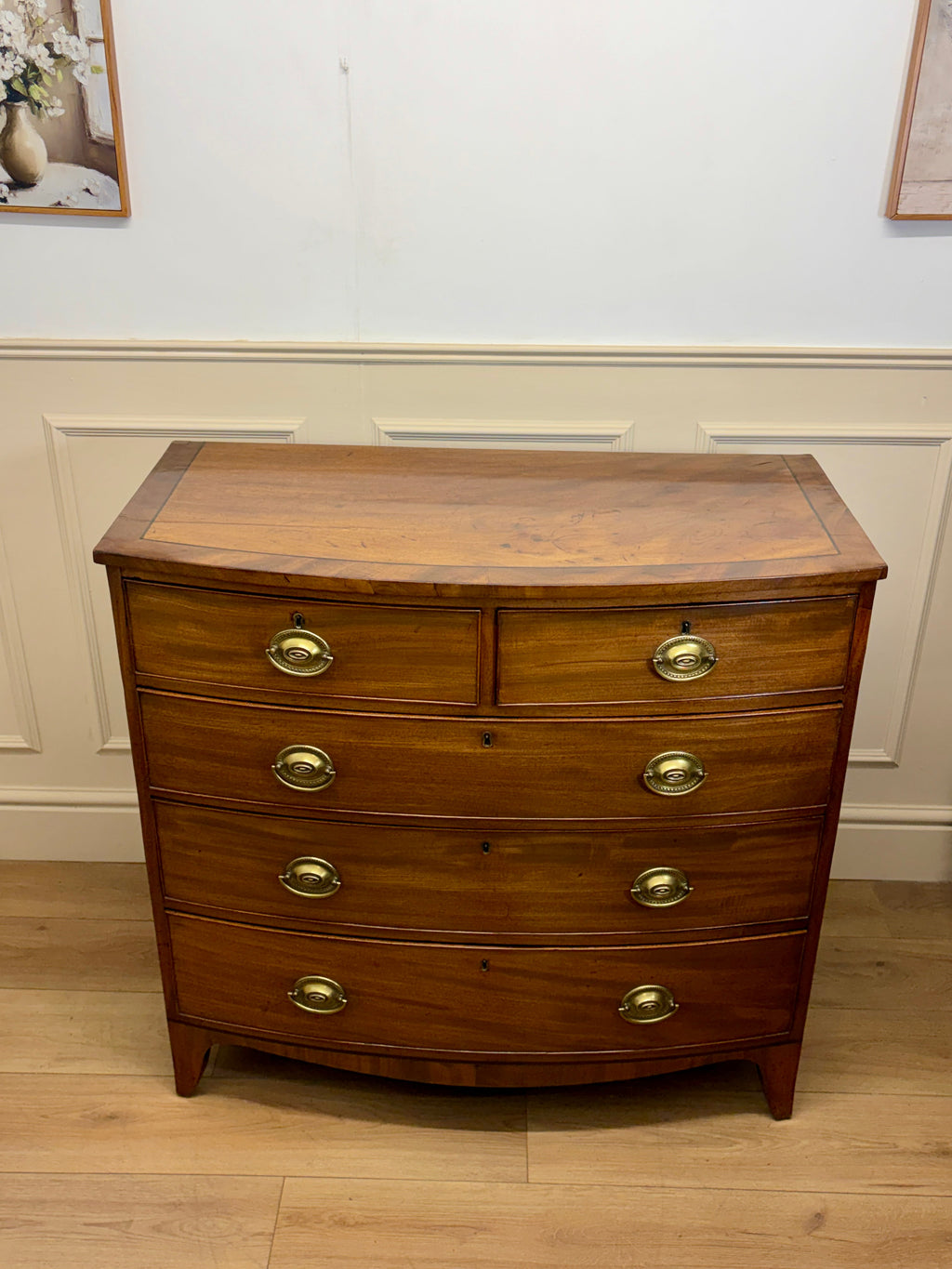 Wooden dresser with curved design and brass handles against a white wall.