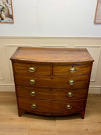 Wooden dresser with curved design and brass handles against a white wall.