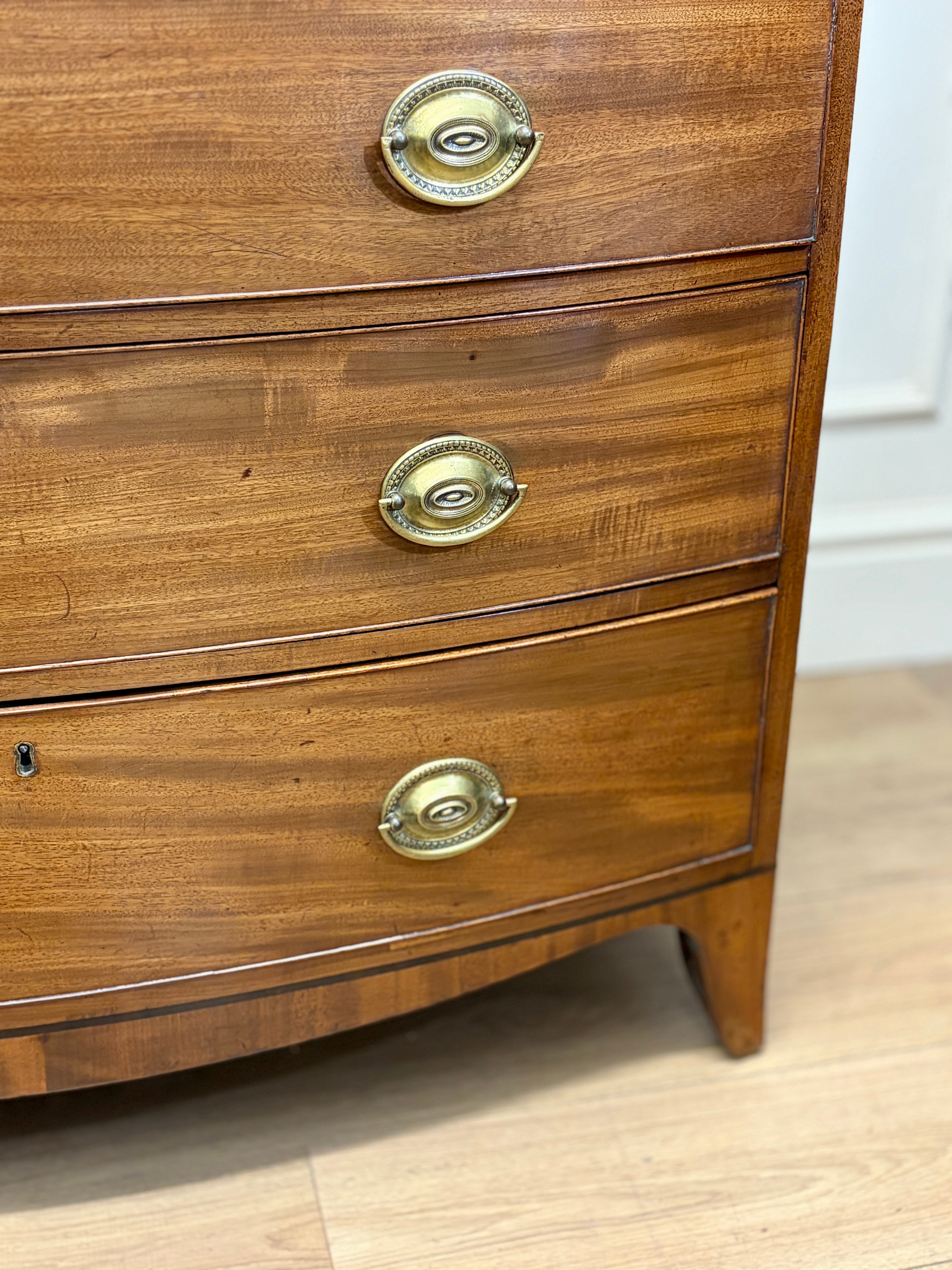 Wooden dresser with brass handles on a light wooden floor.