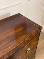 Wooden dresser with a polished surface and brass handles against a white paneled wall.