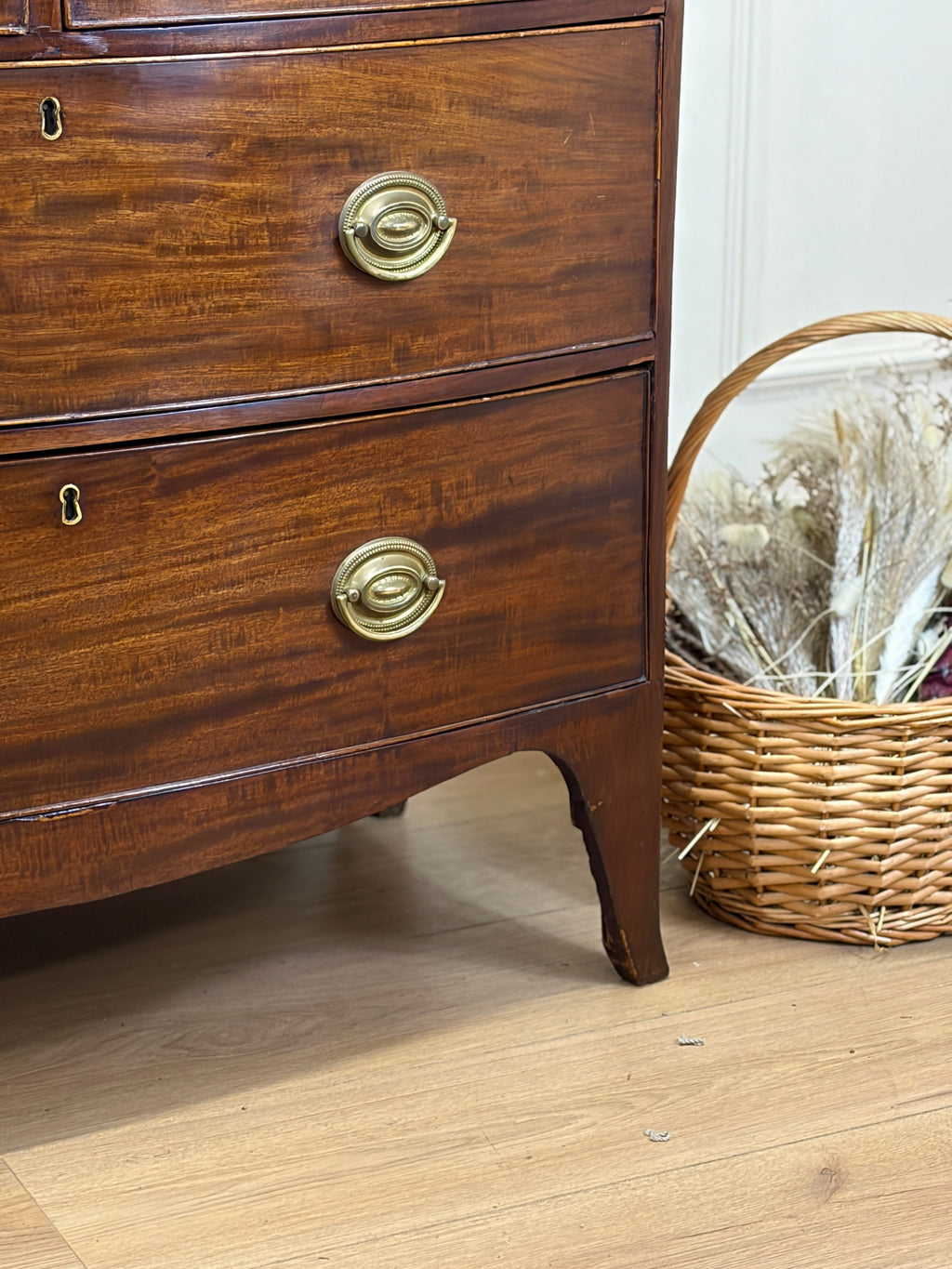 Wooden dresser with brass handles on a wooden floor next to a wicker basket.