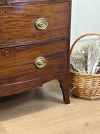 Wooden dresser with brass handles on a wooden floor next to a wicker basket.
