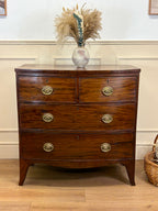 Wooden dresser with four drawers and a vase of pampas grass on top against a white wall.