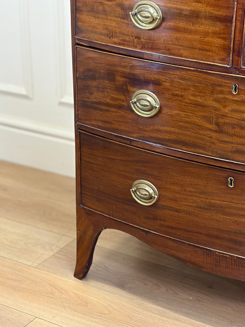 Wooden dresser with brass handles on a wooden floor.