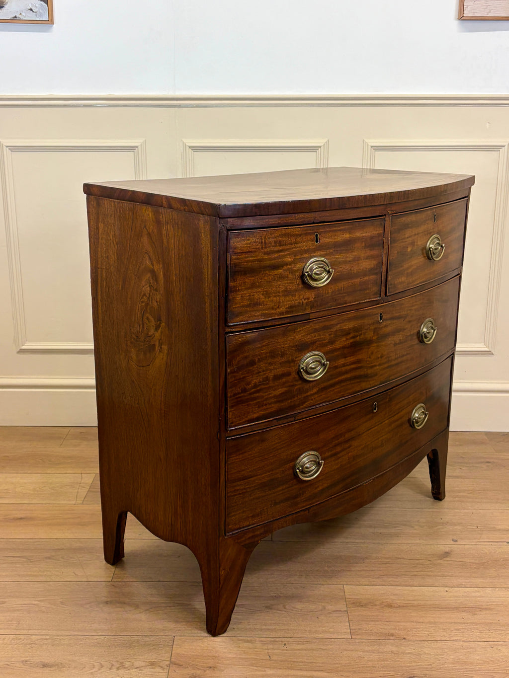 Wooden dresser with three drawers on a wooden floor against a white paneled wall.