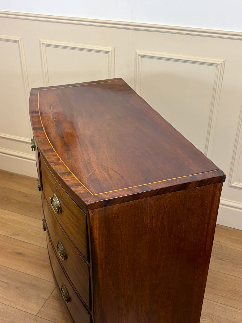 Wooden dresser with curved top against a white paneled wall.