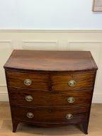 Wooden dresser with four drawers and brass handles against a white wall.