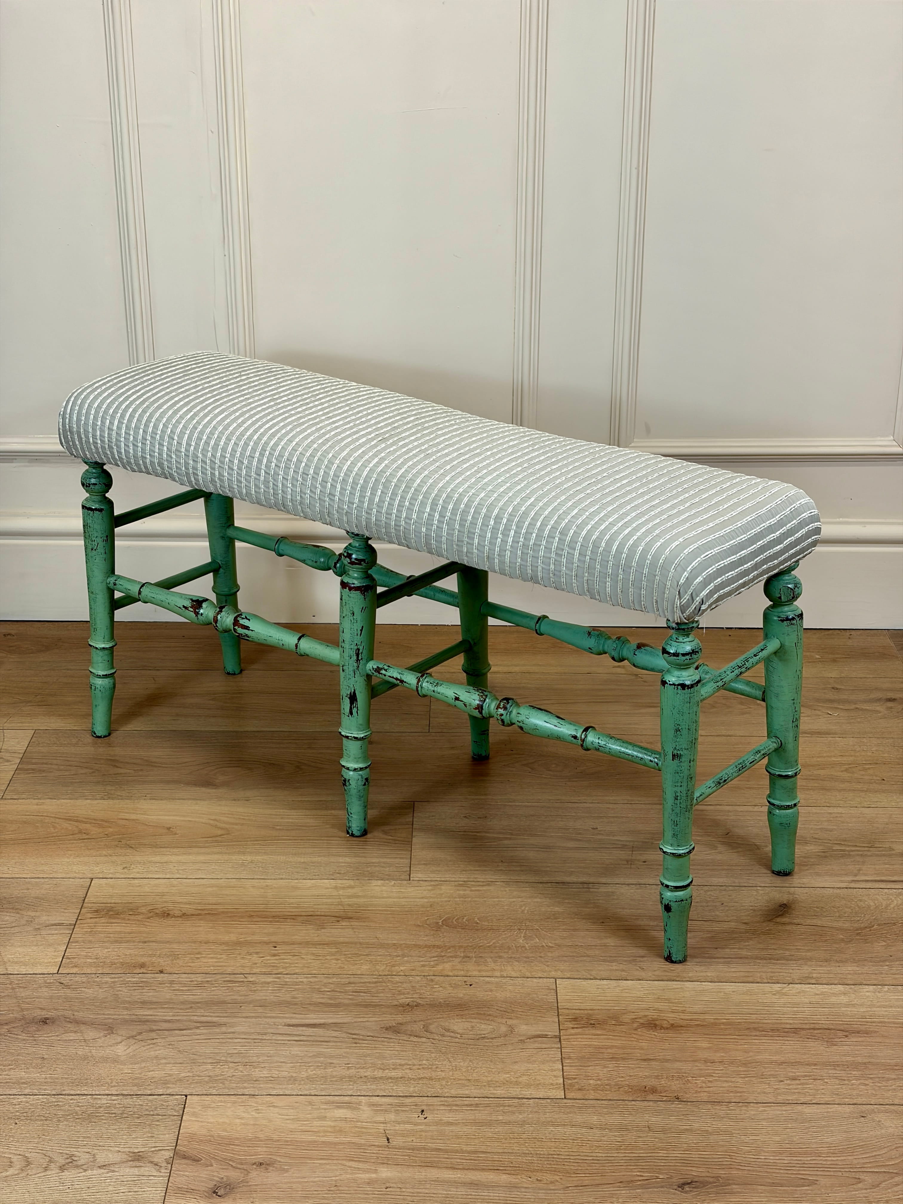 Bench with striped cushion on a wooden floor against a paneled wall.