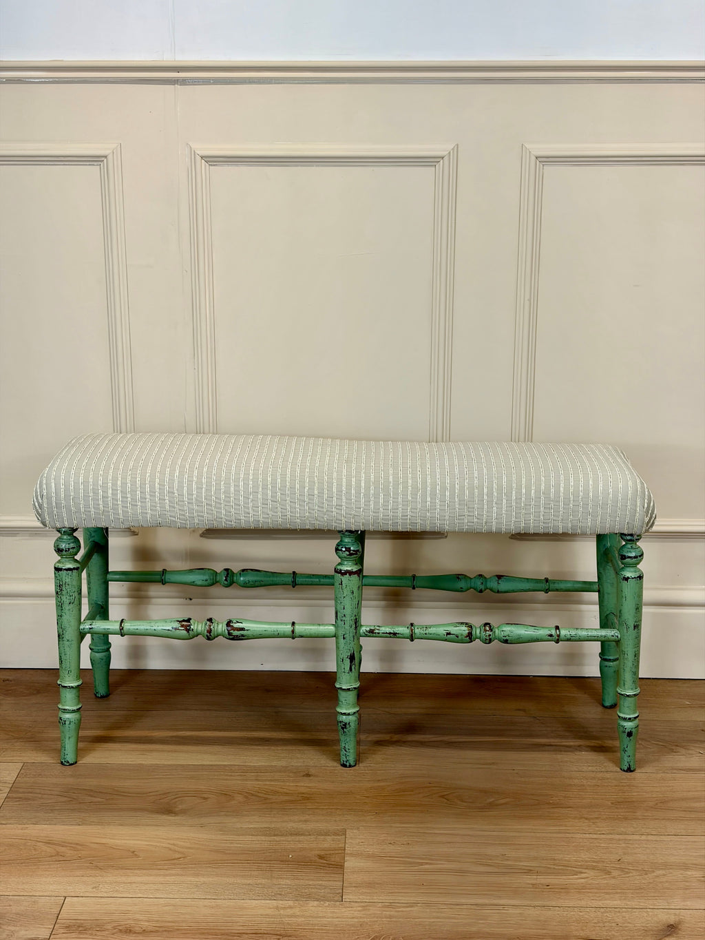 Green-finished bench with striped cushion against a paneled wall.