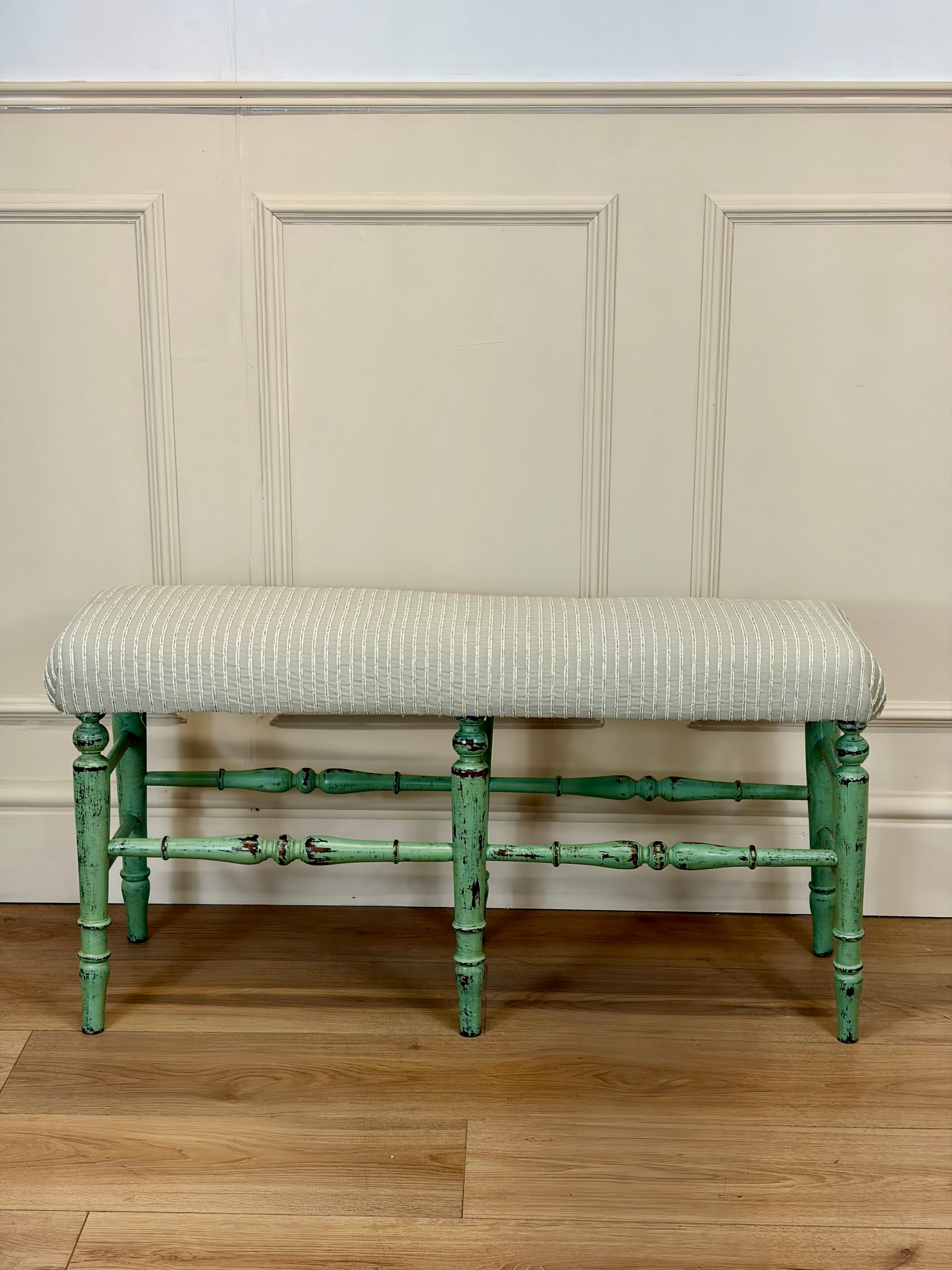 Green-finished bench with striped cushion against a paneled wall.