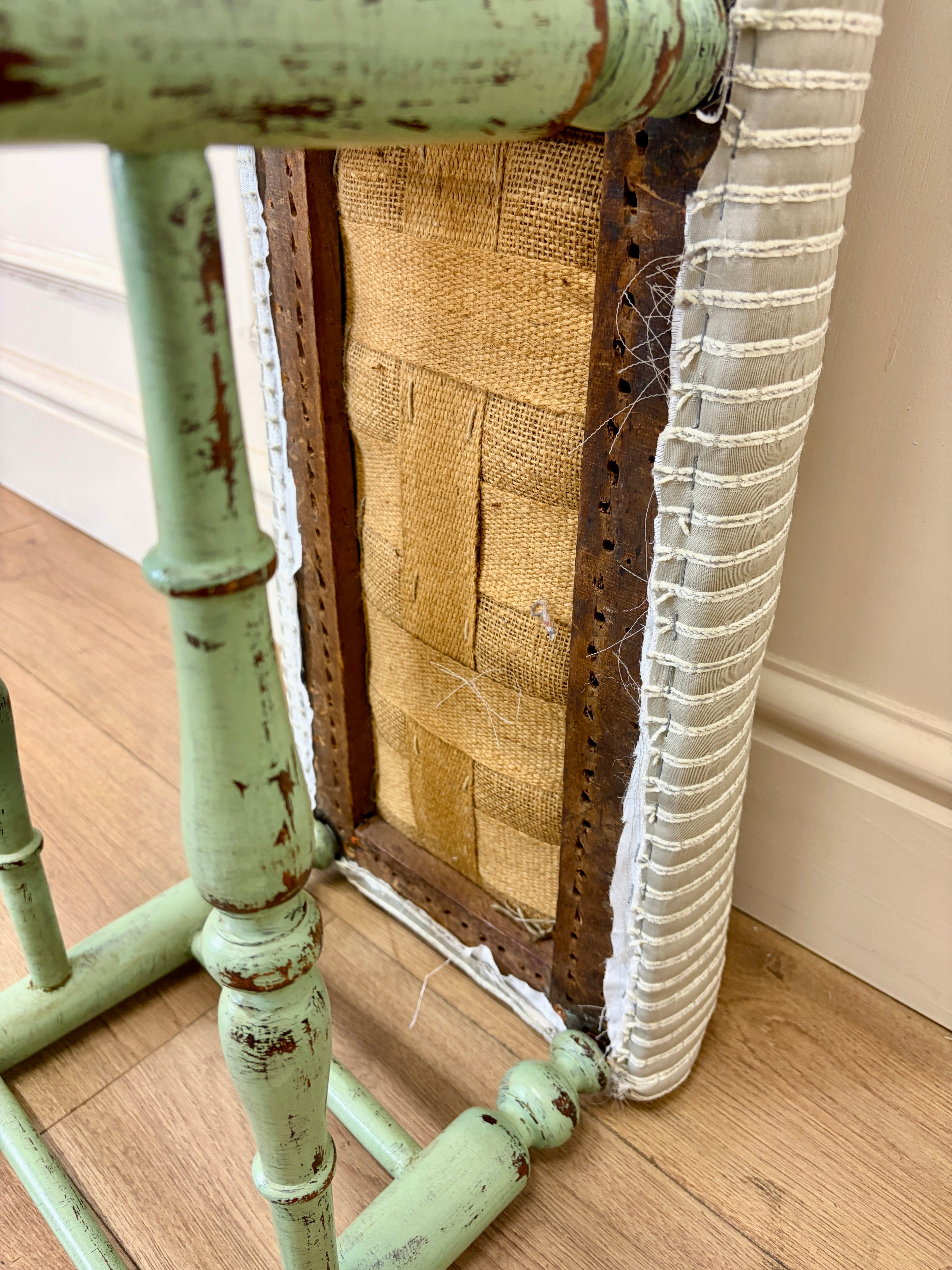 Vintage green stool with a textured white cushion and burlap fabric on a wooden floor.