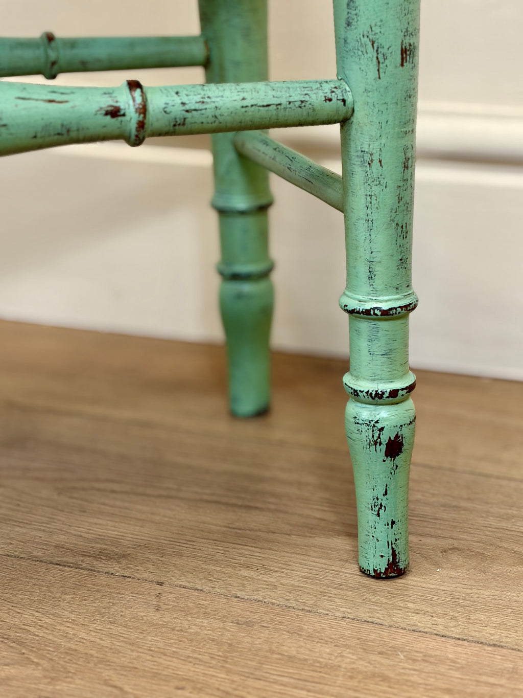 Close-up of a green bamboo-style chair leg on a wooden floor.