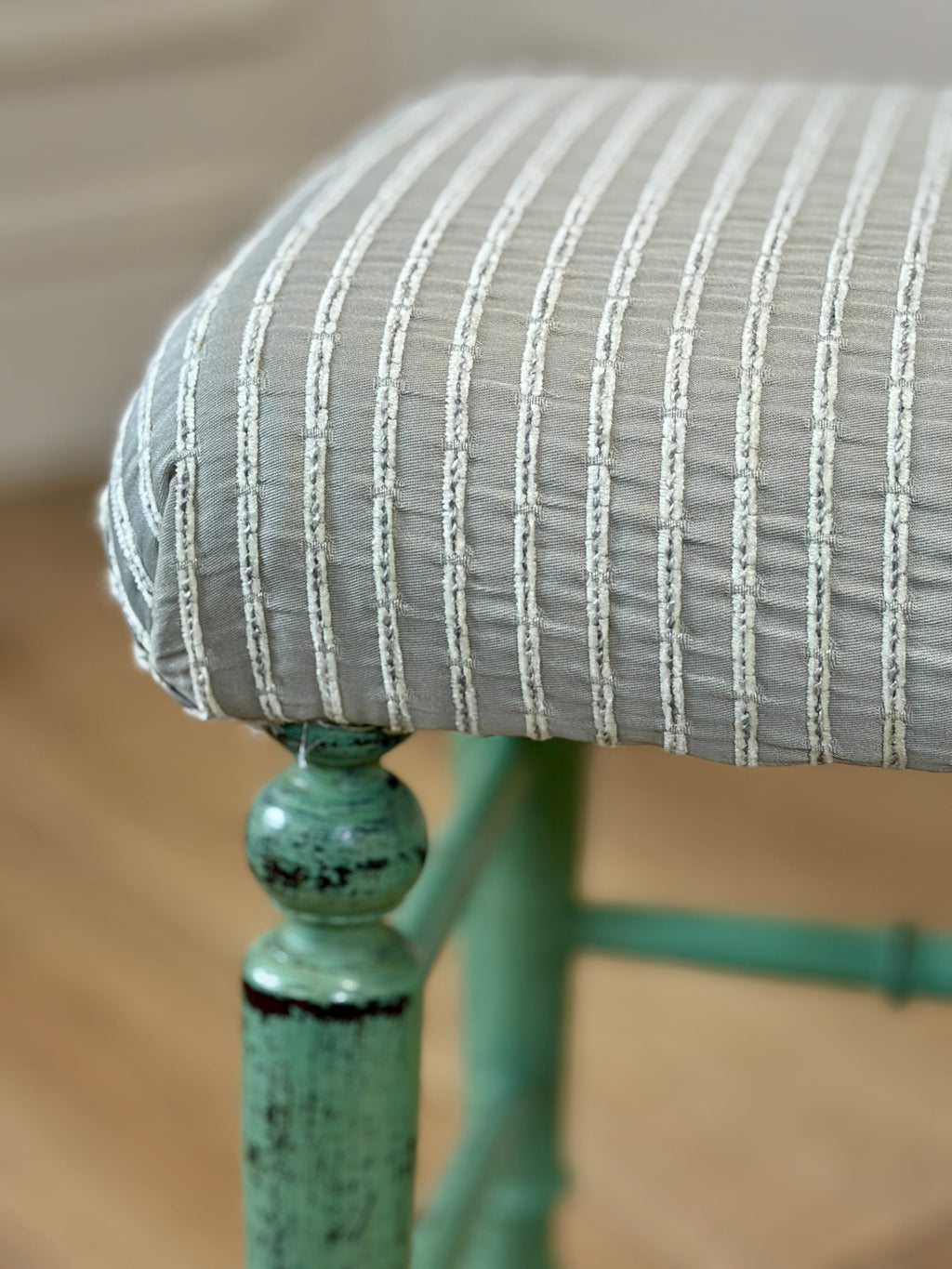 Close-up of a chair with a striped cushion and green metal frame.