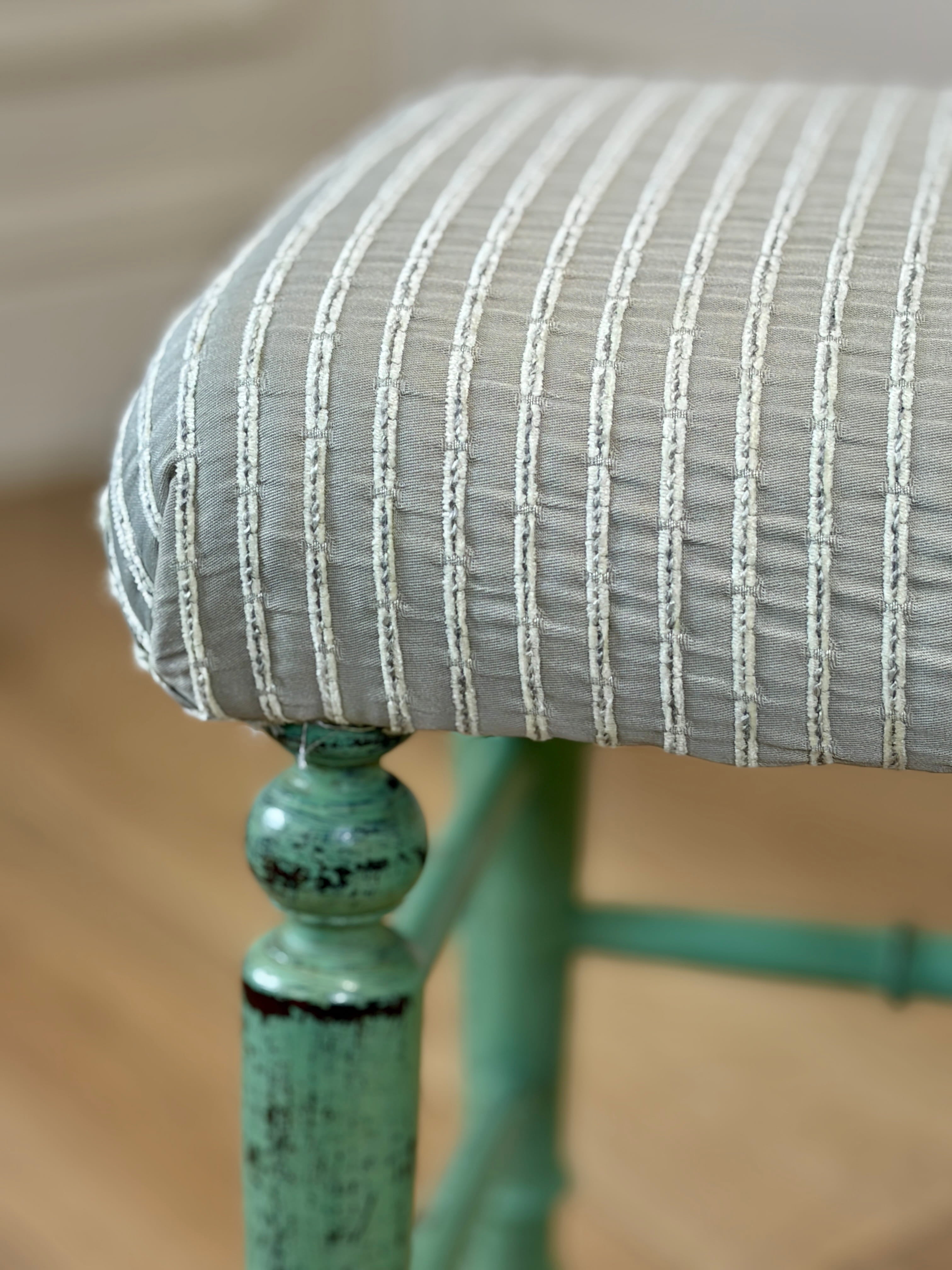 Close-up of a chair with a striped cushion and green metal frame.