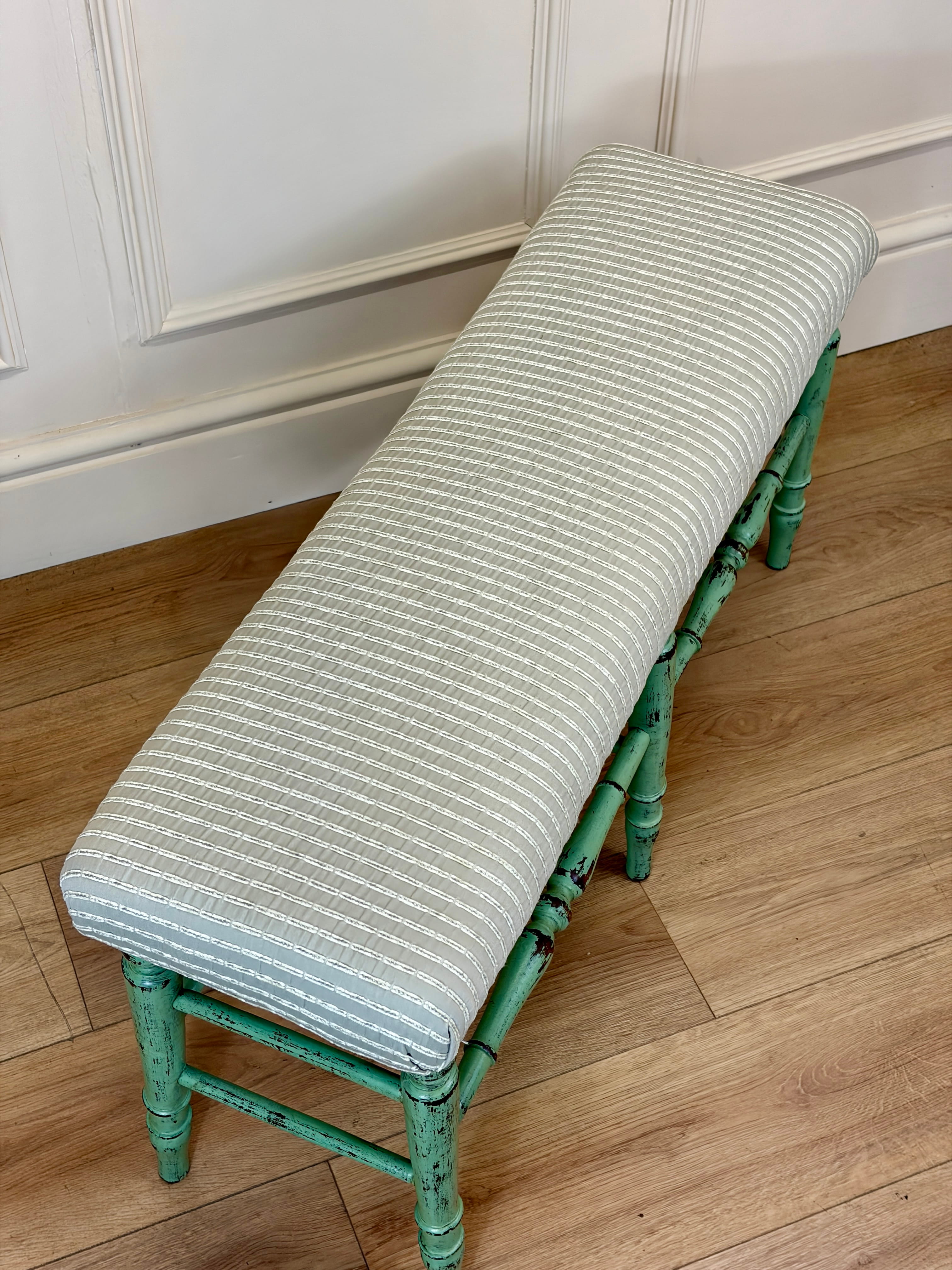 Green bench with a striped cushion on a wooden floor against a white paneled wall.