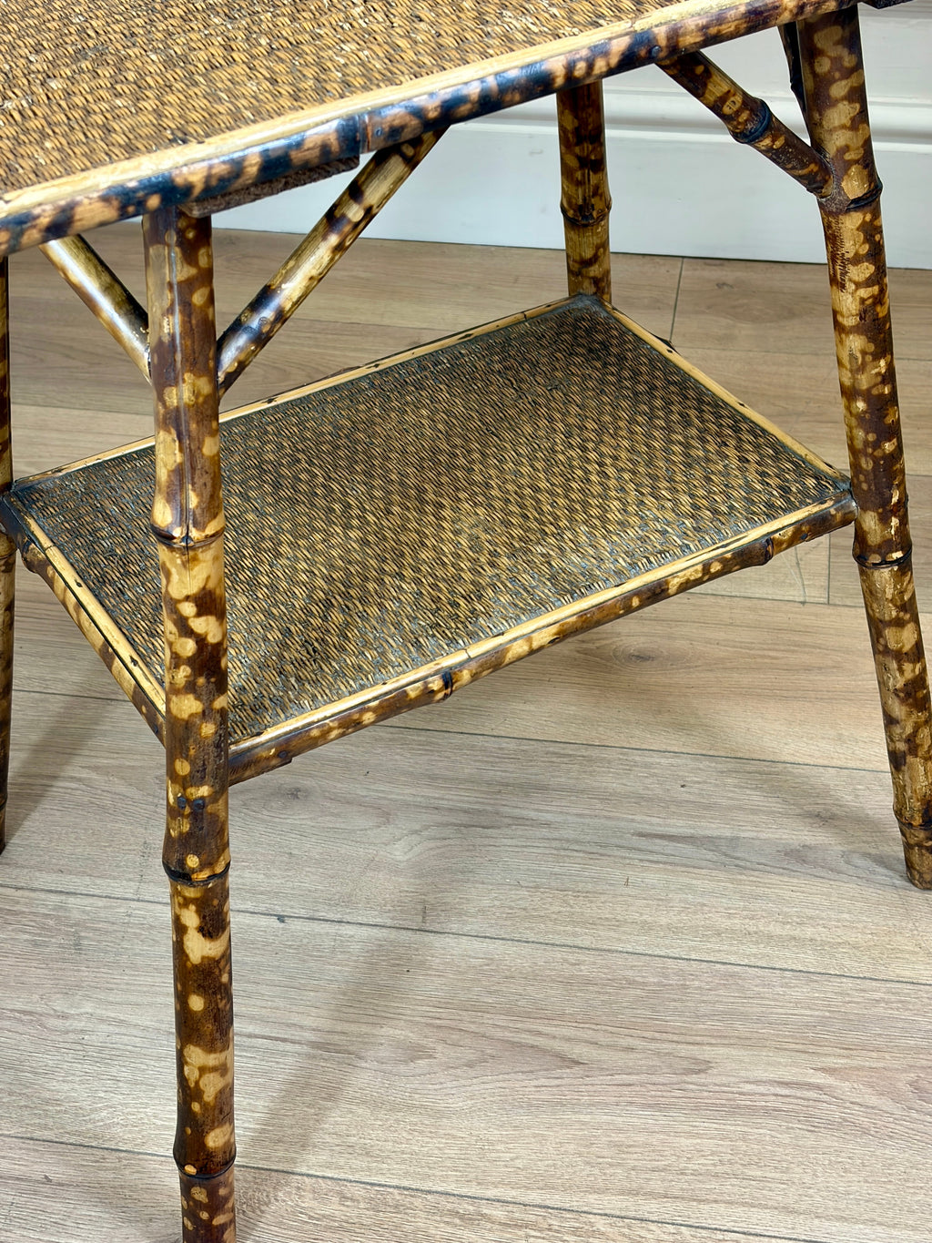 Bamboo side table with woven shelves on a wooden floor.