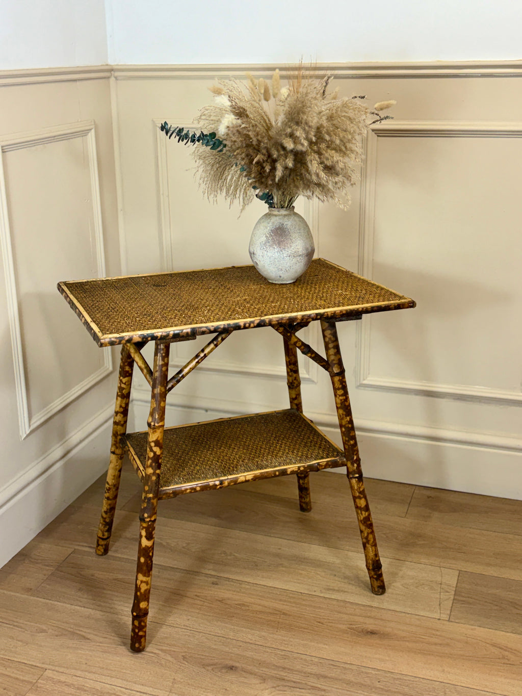 Rattan side table with a vase of dried flowers against a neutral wall.