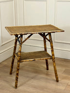 Bamboo side table with woven top and shelf against a white paneled wall.