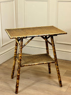 Wicker side table with a shelf against a white paneled wall.
