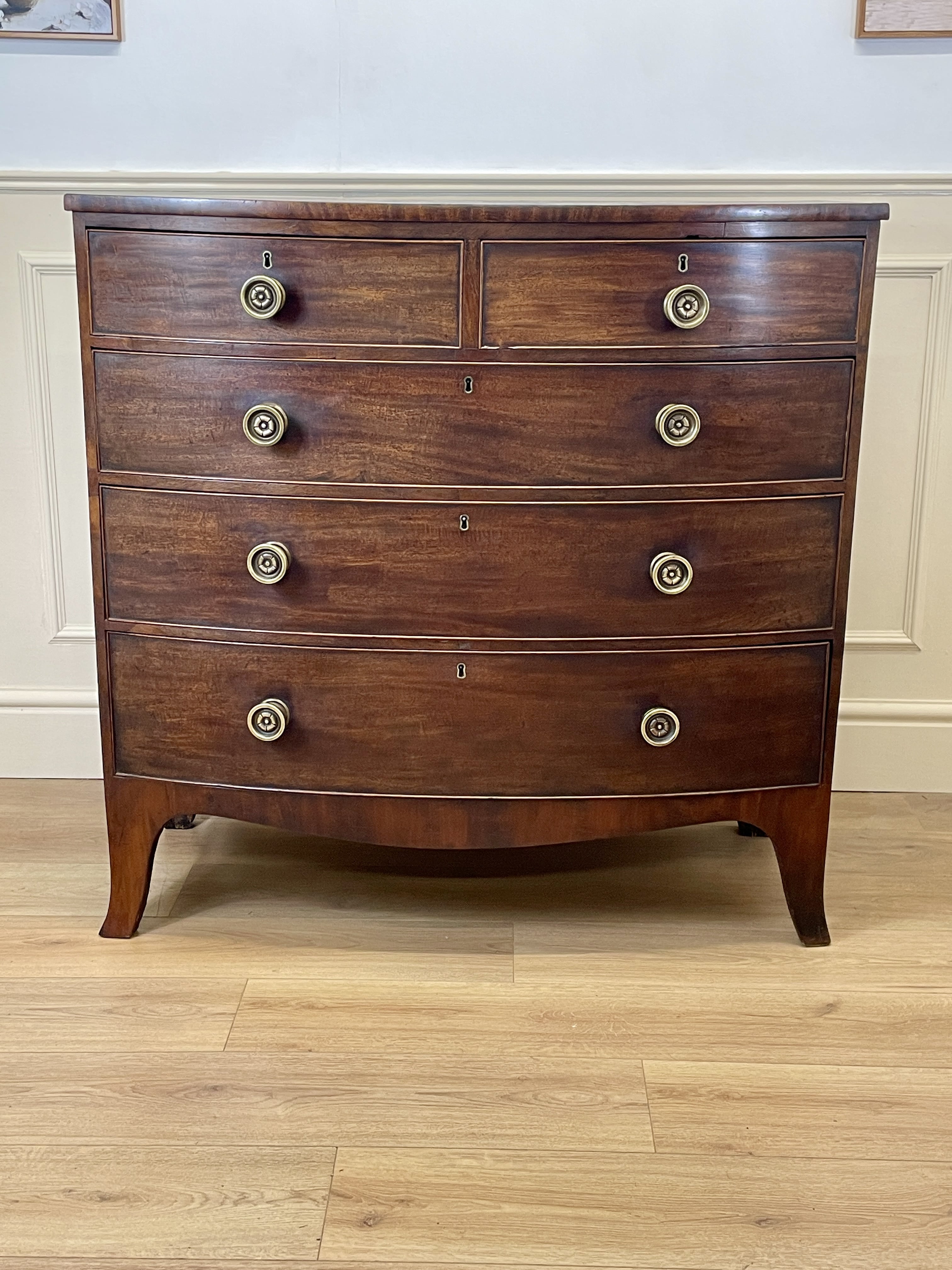Wooden dresser with four drawers on a wooden floor against a white wall.