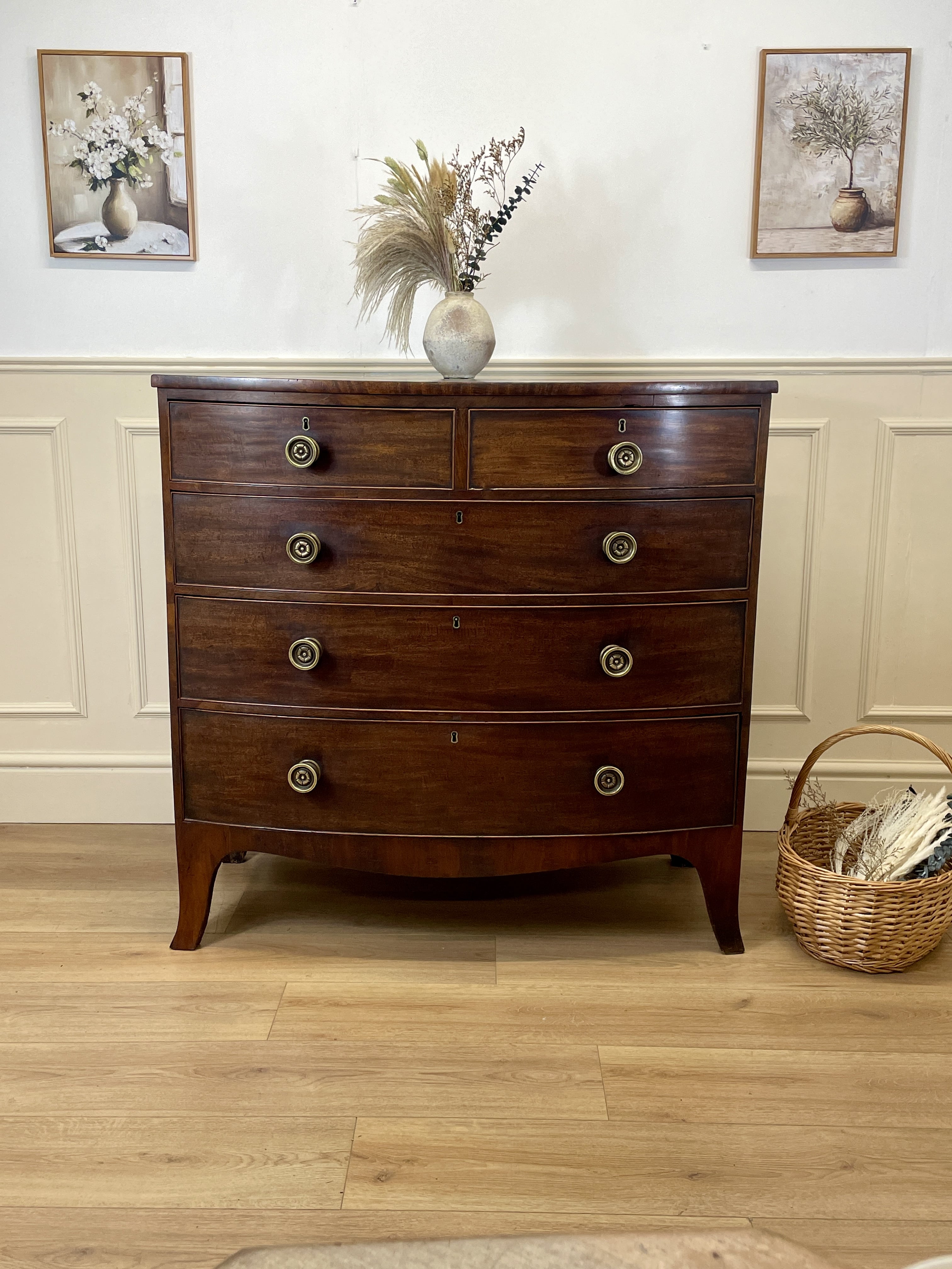 Wooden dresser with decorative items in a room with wainscoting and framed pictures.