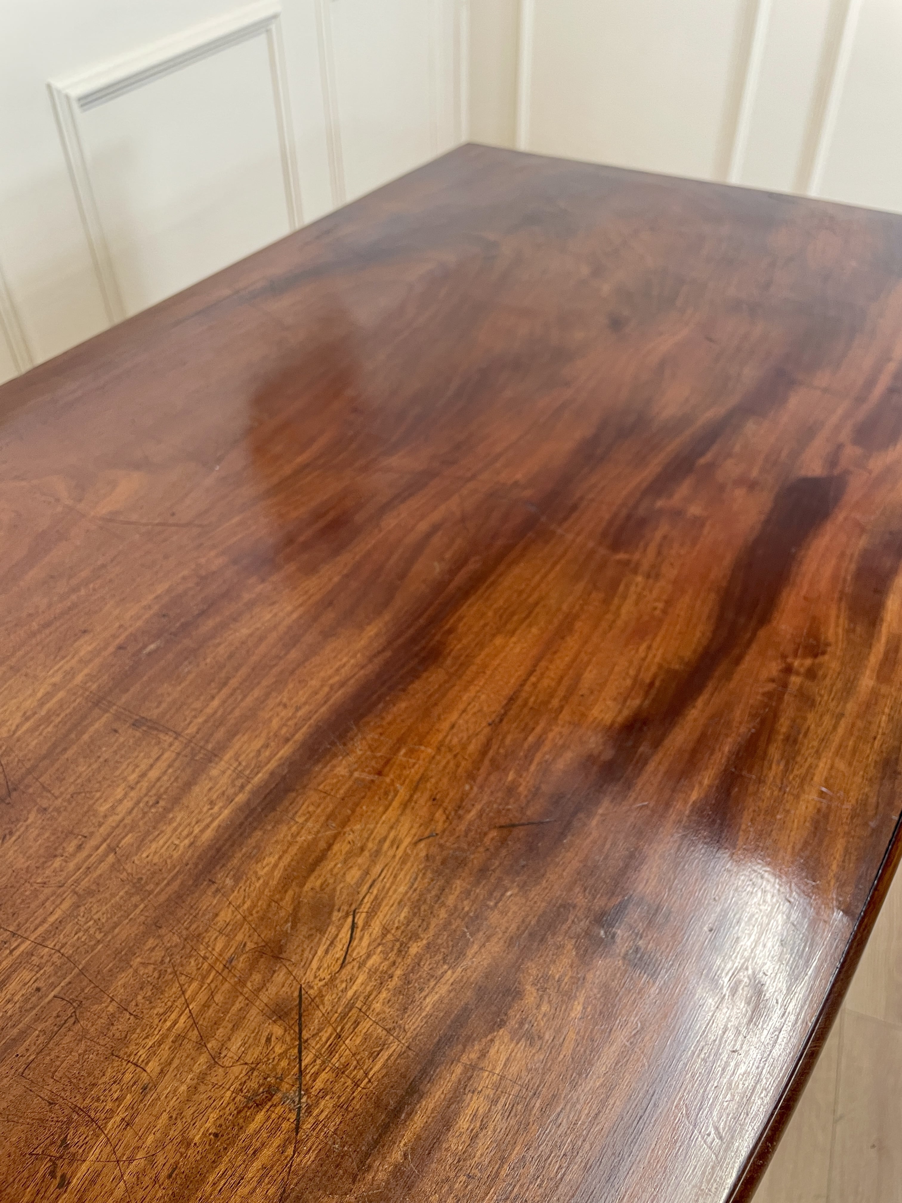 Wooden table with a glossy finish in a room with white walls and a chair.
