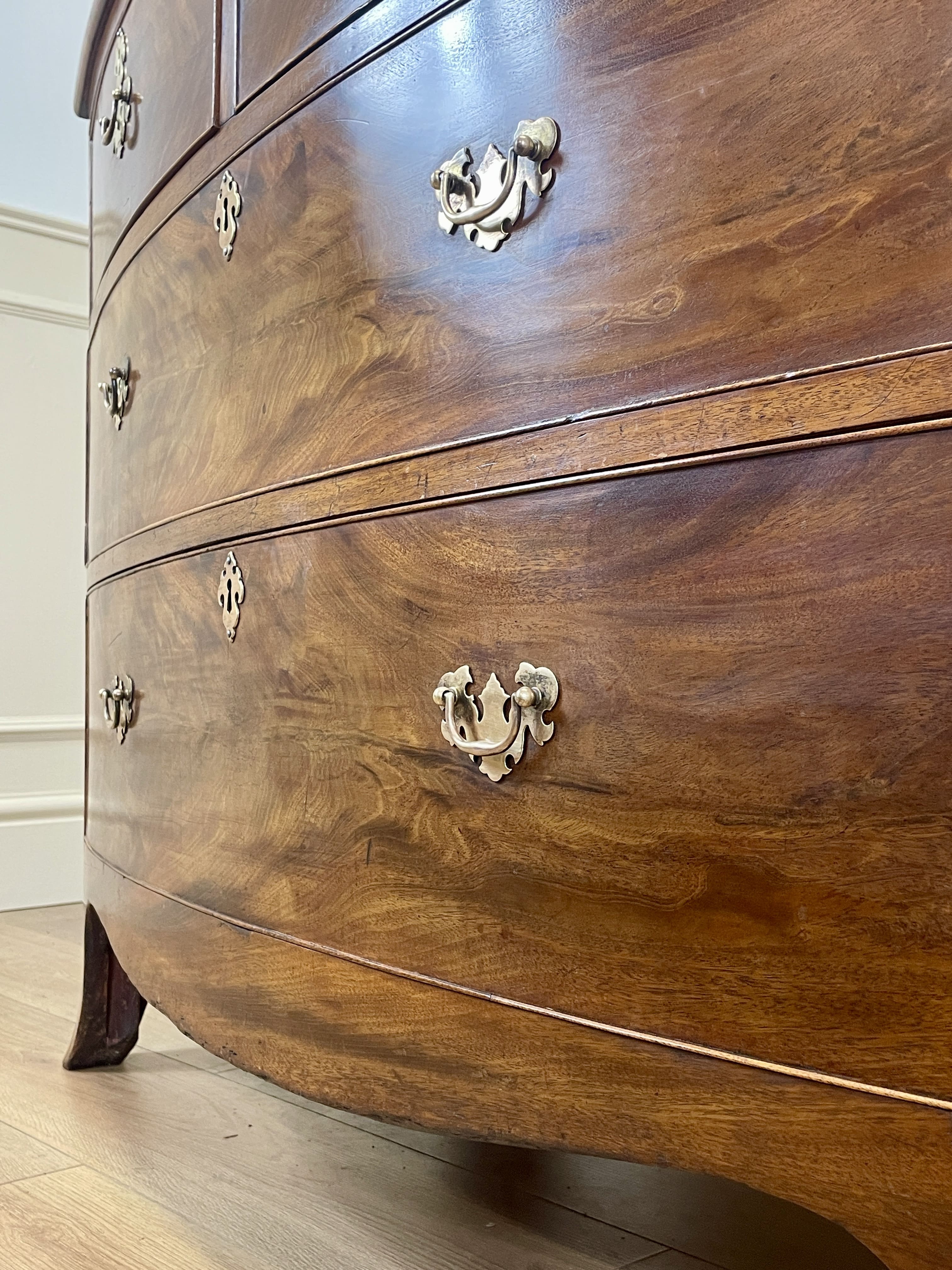 Wooden dresser with curved design and decorative handles on a wooden floor.