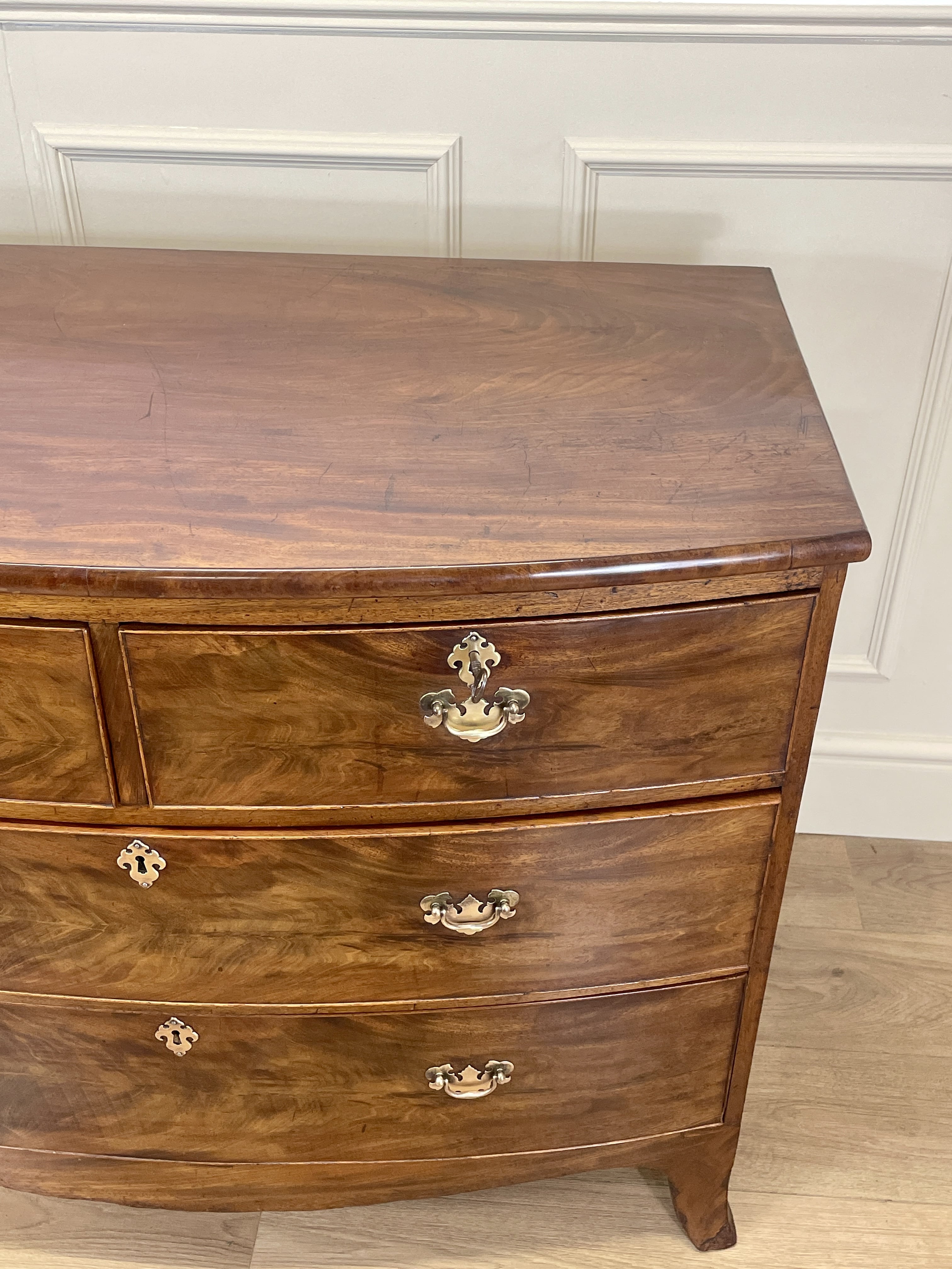 Wooden dresser with curved design and brass handles against a white paneled wall.