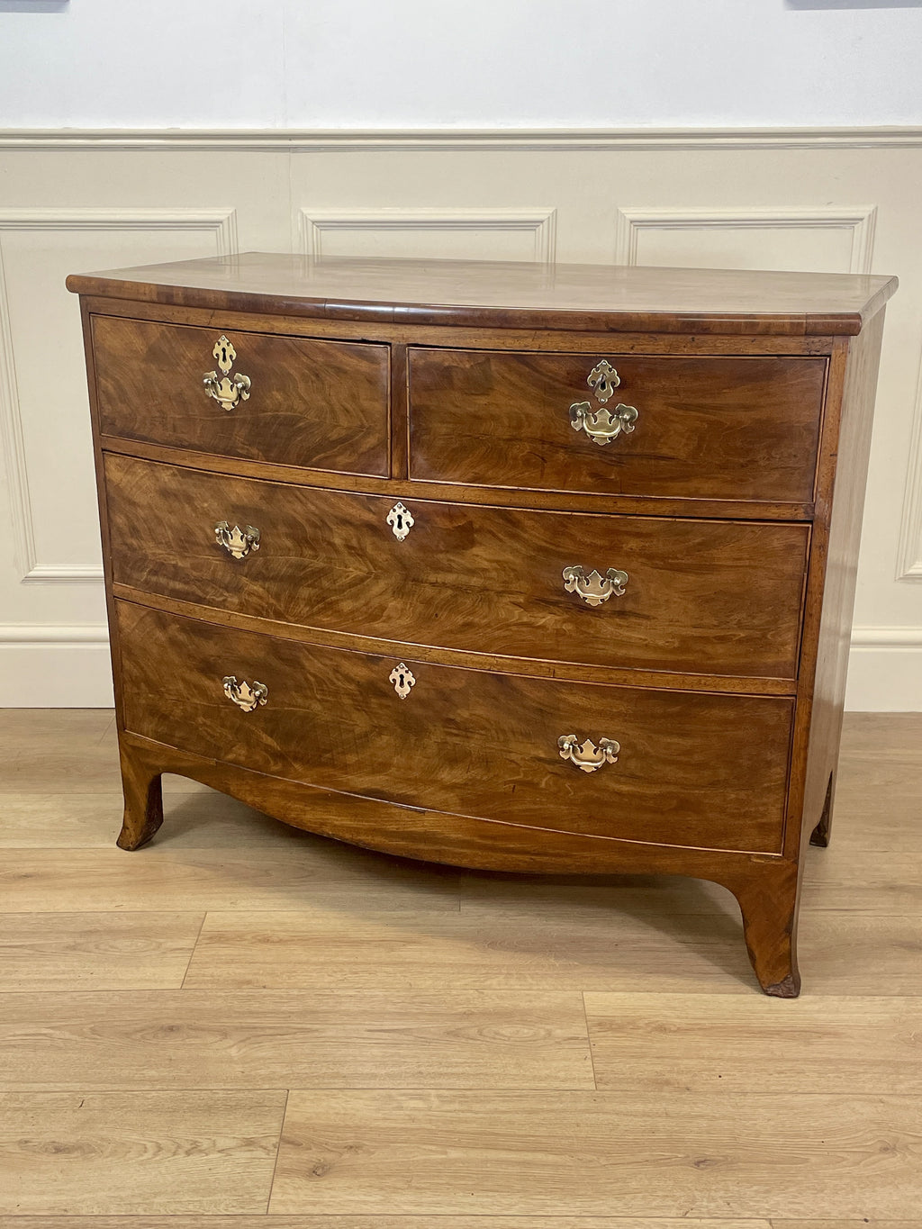 Wooden dresser with four drawers on a wooden floor against a white wall.