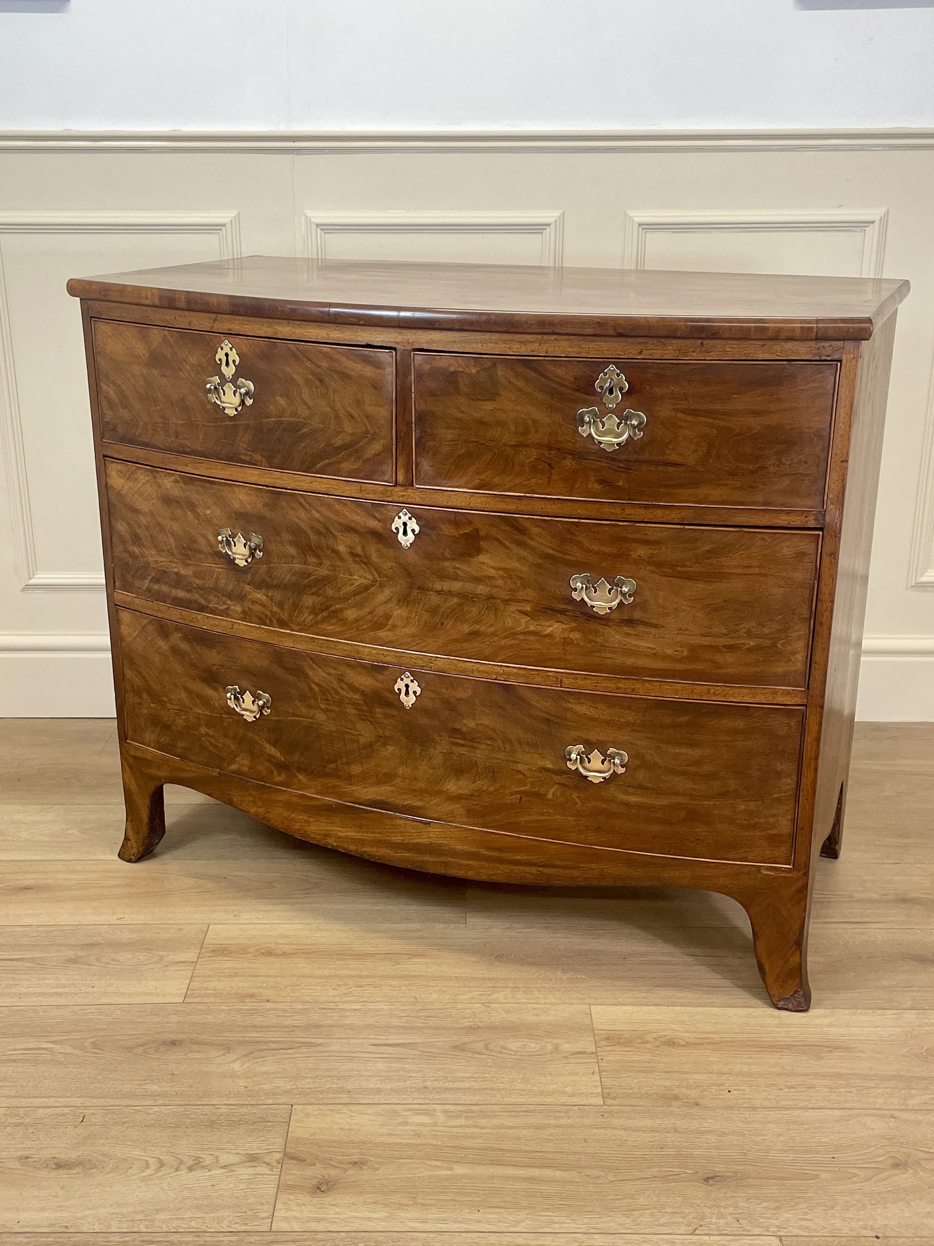 Wooden dresser with four drawers on a wooden floor against a white wall.