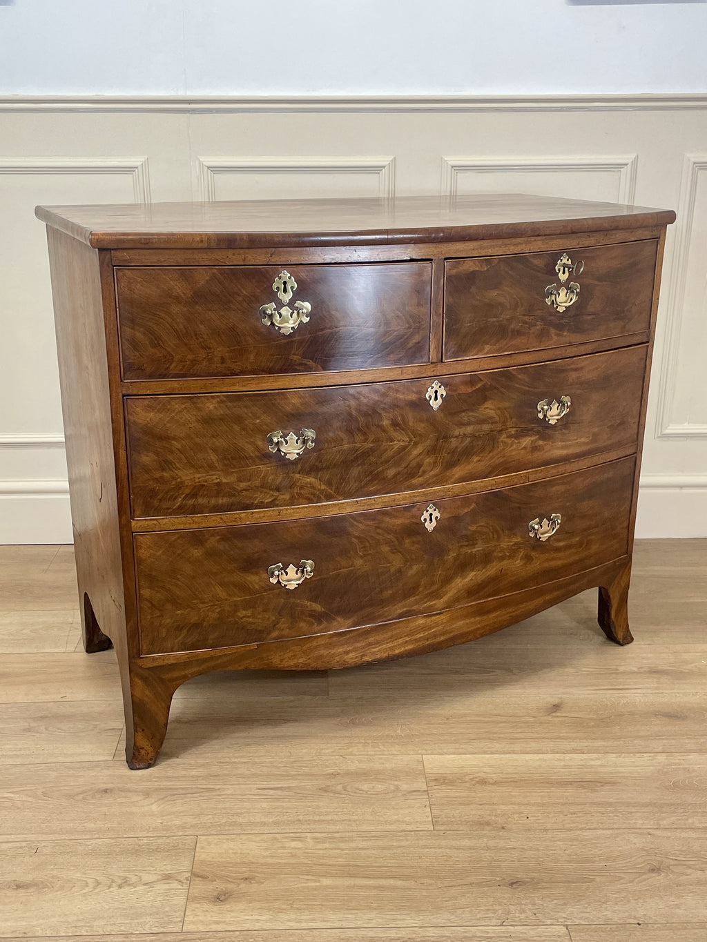Wooden dresser with four drawers on a wooden floor against a white wall.