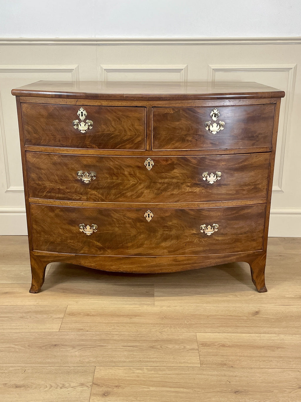 Wooden dresser with four drawers on a wooden floor against a white wall.
