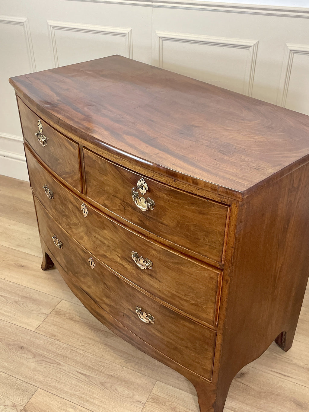 Wooden dresser with four drawers on a wooden floor against a white paneled wall.