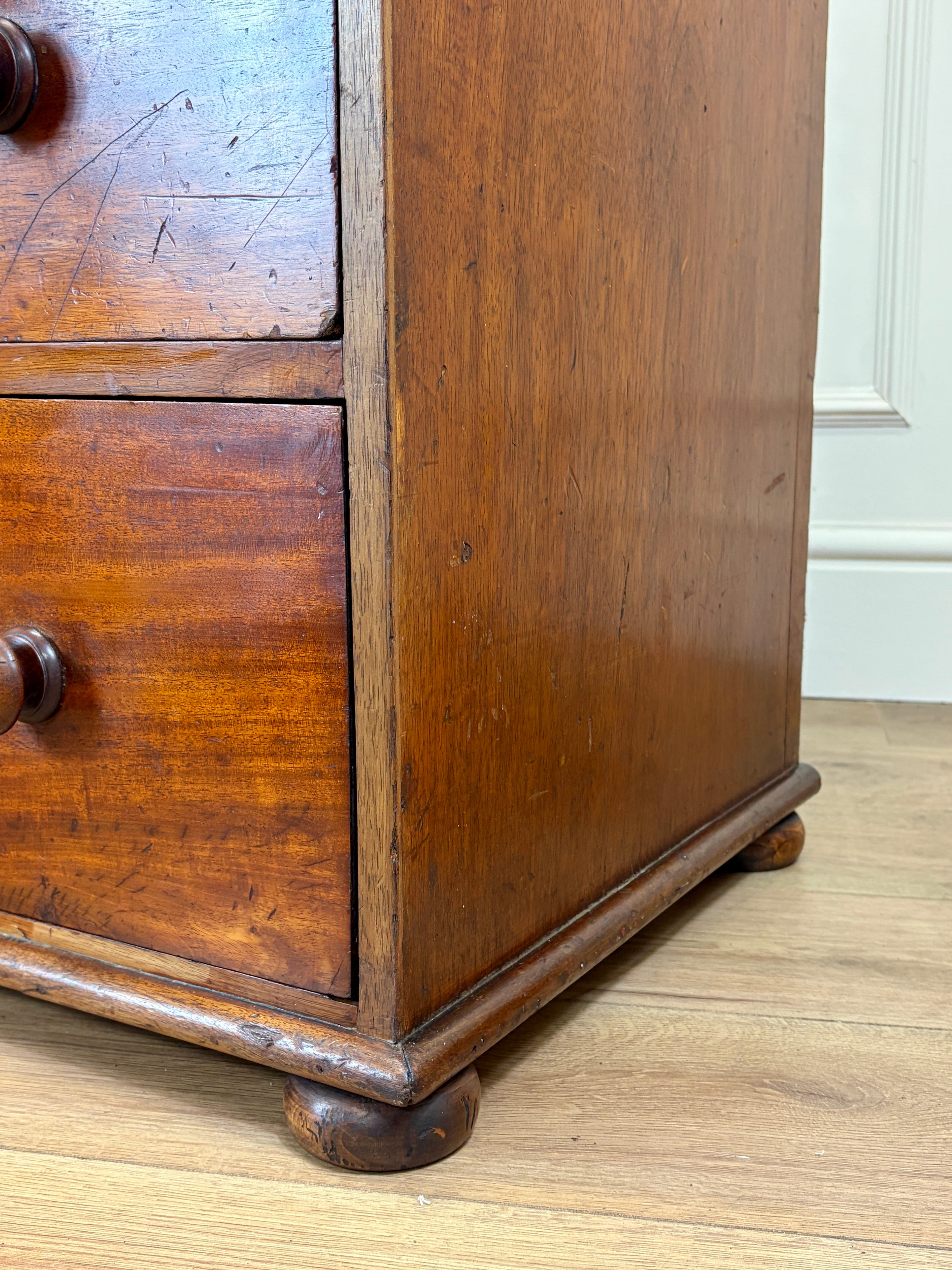 Close-up of an old wooden dresser with visible wear on a wooden floor.