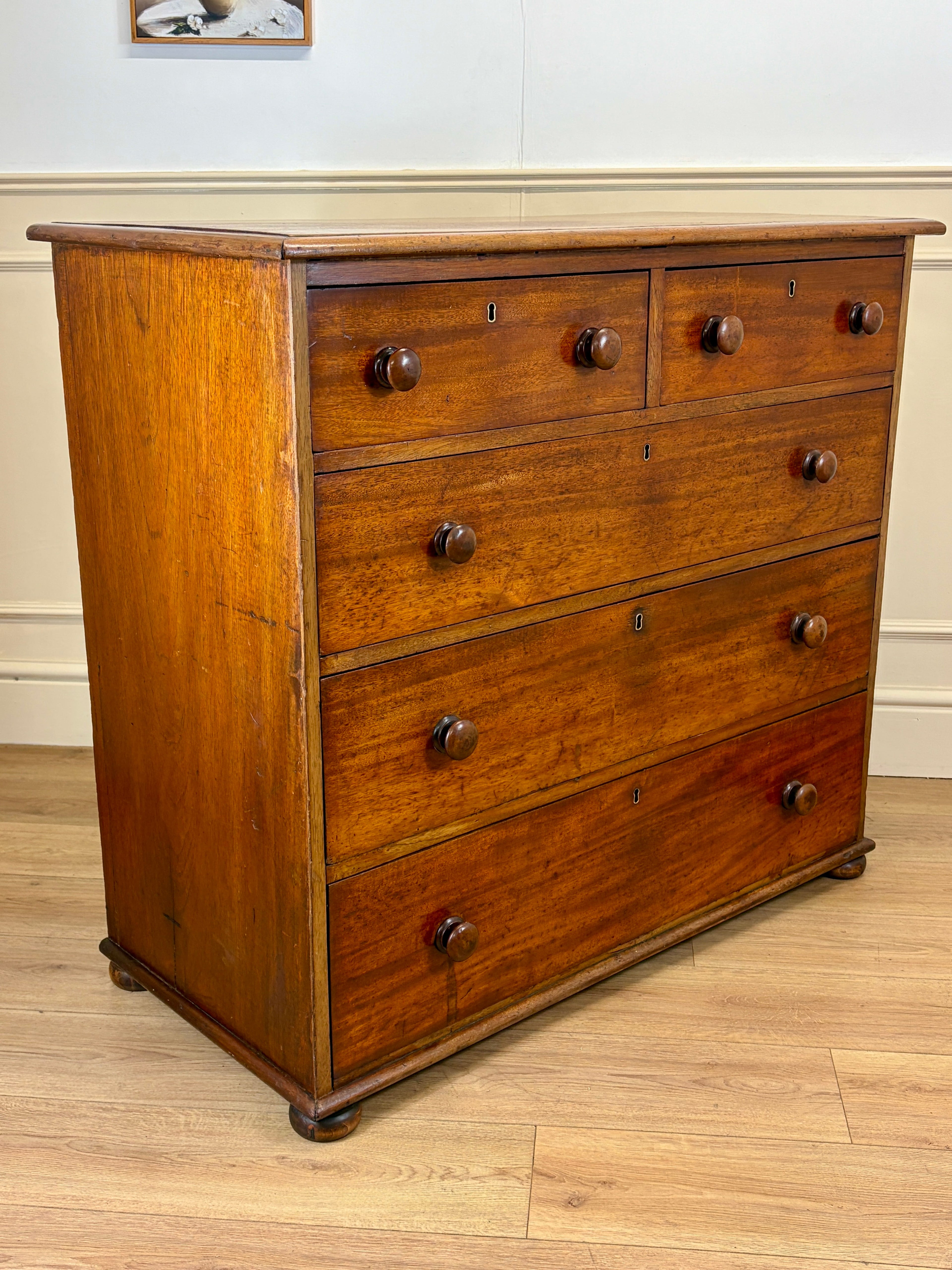 Wooden dresser with four drawers on a wooden floor against a white wall.