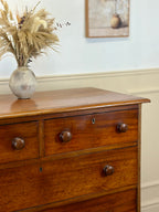 Wooden dresser with a vase of dried plants on top against a light blue wall.