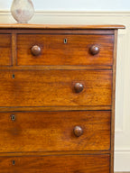 Wooden dresser with three drawers and metal knobs against a white wall.