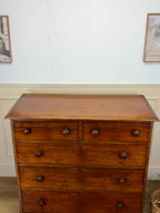 Wooden dresser with four drawers against a white wall.