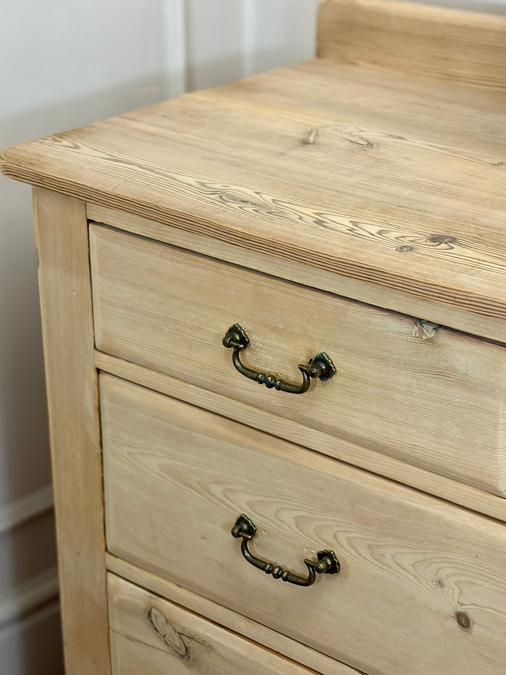 Wooden dresser with two drawers and metal handles against a white wall.