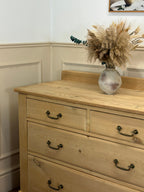 Wooden dresser with a vase of dried flowers on top against a white wall.