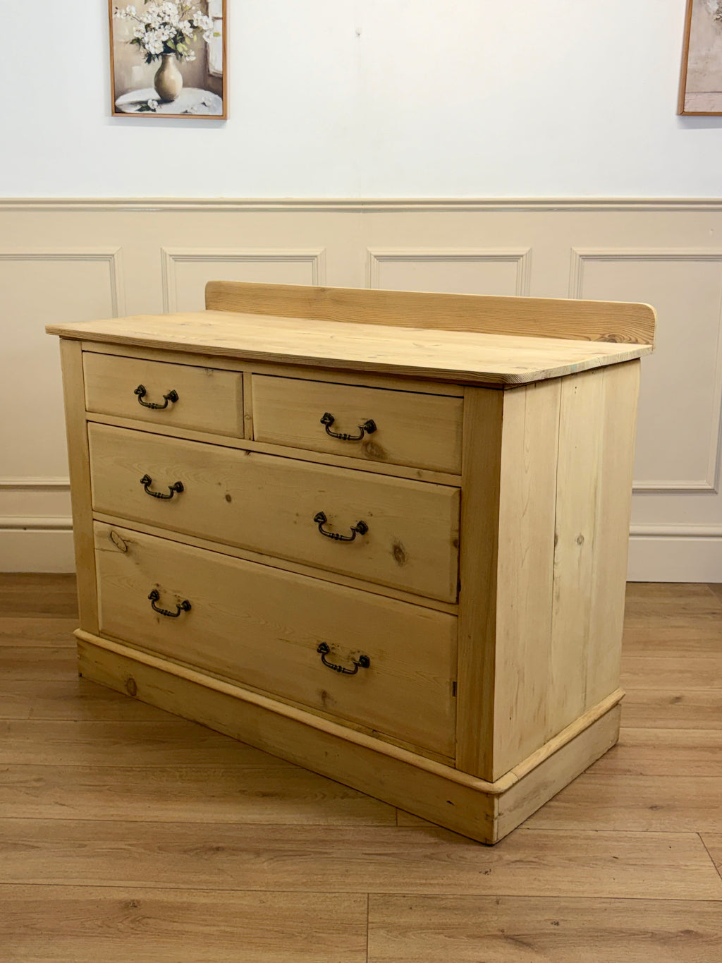 Wooden dresser with four drawers in a room with white walls and wooden flooring.