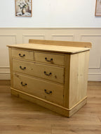 Wooden dresser with four drawers in a room with white walls and wooden flooring.