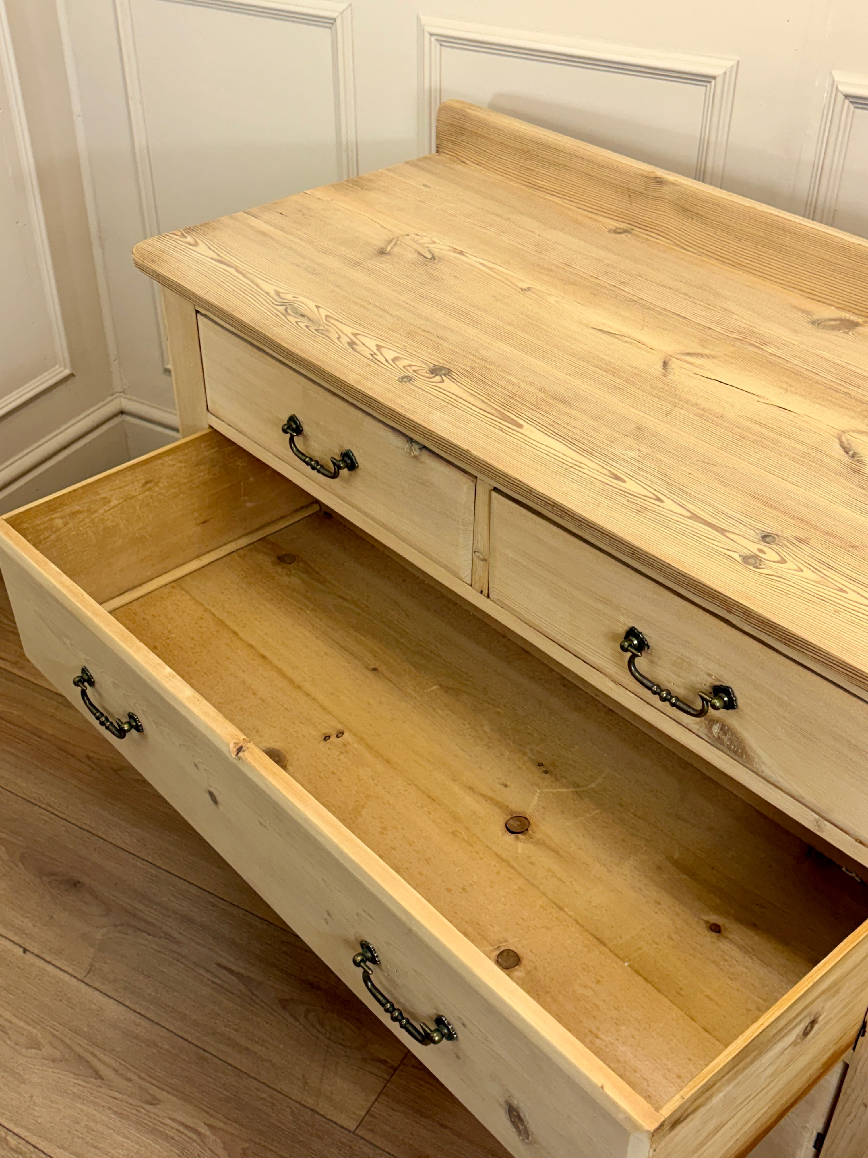 Wooden dresser with open drawer against a white paneled wall.