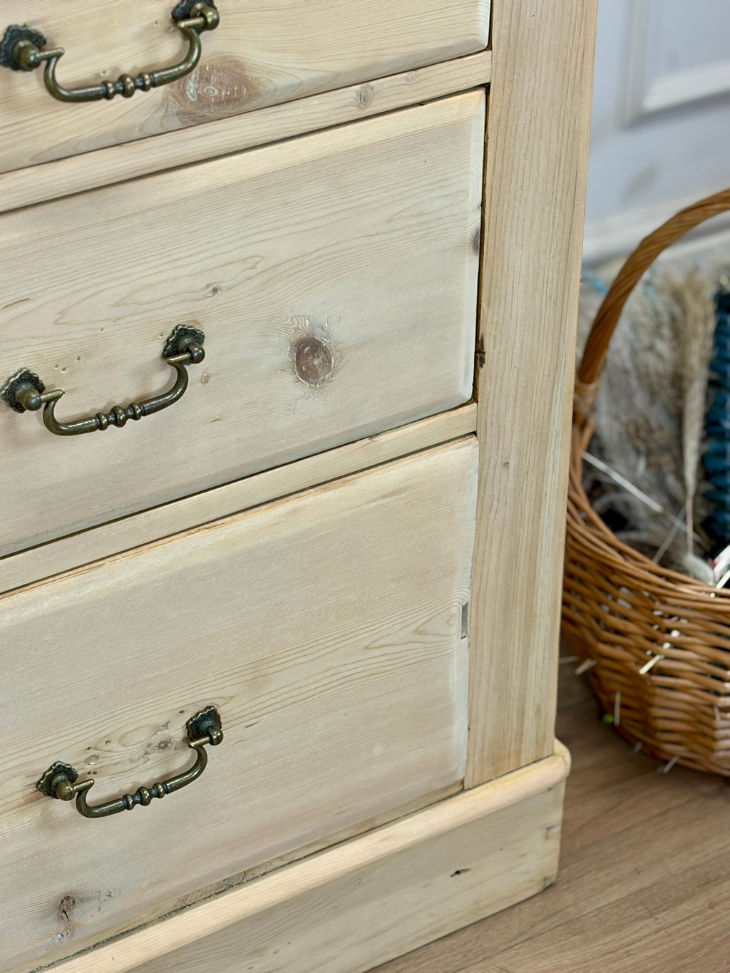 Wooden dresser with three drawers and metal handles, next to a wicker basket.
