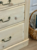 Wooden dresser with three drawers and metal handles, next to a wicker basket.