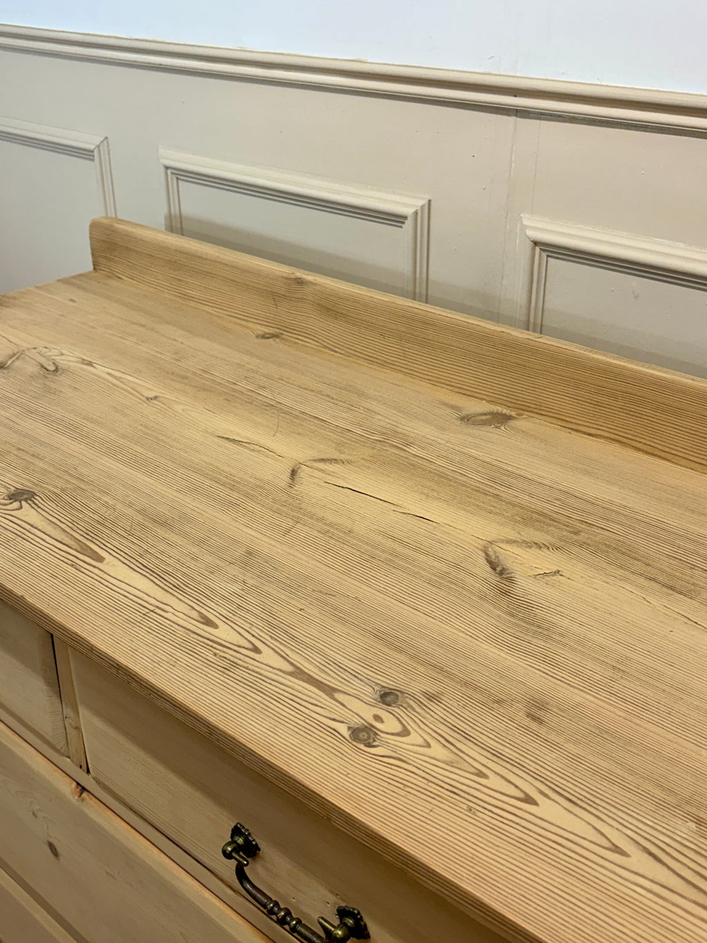 Wooden dresser with a light finish and black handle against a neutral wall.