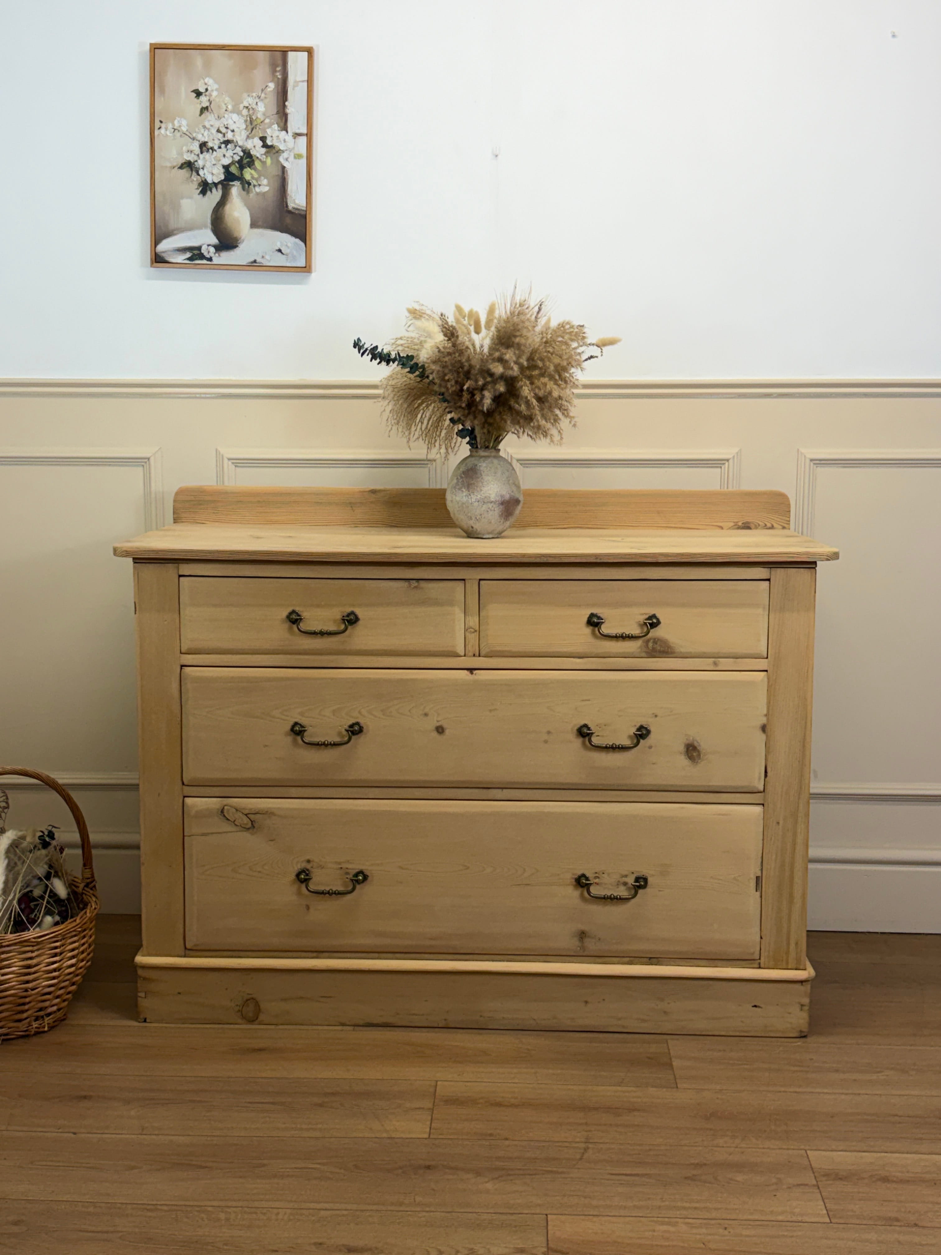 Wooden dresser with four drawers in a room with a painting and vase on the wall.