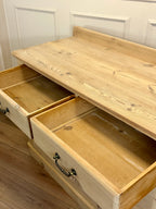 Wooden dresser with open drawers against a white paneled wall.