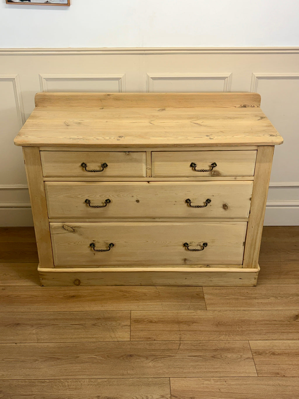 Wooden dresser with four drawers on a wooden floor against a white wall.