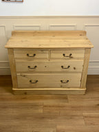 Wooden dresser with four drawers on a wooden floor against a white wall.